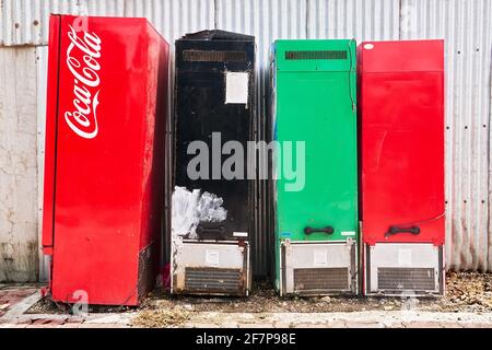 Close-up view of multicolored old and rusty refrigerators placed in a row next to a corrugated metal wall, seen along a road in the Philippines, Asia Stock Photo