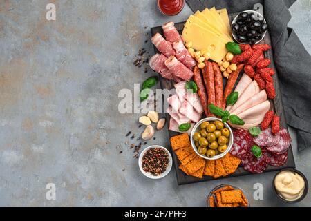 Meat delicacies, cheese, olives, sauces and crackers on a gray background with space to copy. Top view, horizontal. Stock Photo