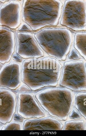 The texture of a concrete wall in the style of a swamp-colored snake skin, paved with large cobblestones. Close-up. Stock Photo