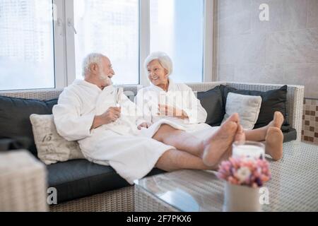 Senior couple in white robes having great times in spa salon and looking relaxed Stock Photo
