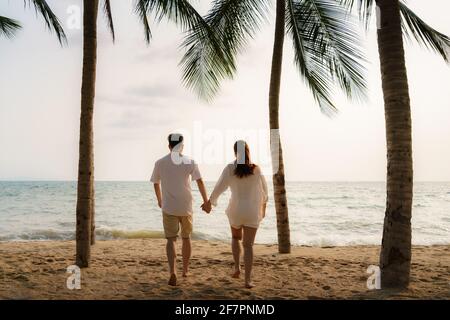 Asian couple is running and holding hands on a beachfront beach sea with coconut trees while on vacation in the summer in Thailand. Stock Photo