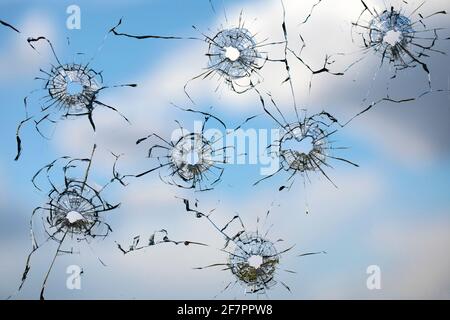 holes and cracks from bullets in glass, on sky background Stock Photo