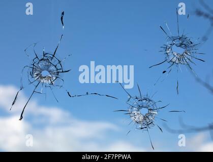 holes and cracks from bullets in glass, on sky background Stock Photo