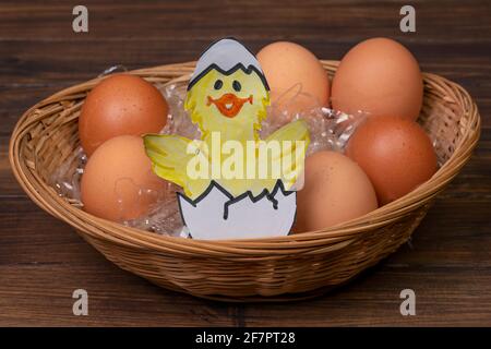 A funny drawn chick hatches out of the egg in a basket of real eggs in the straw Stock Photo