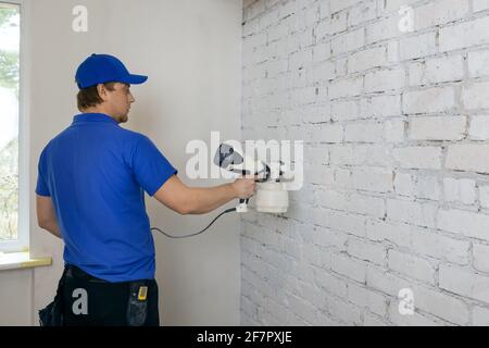 man painting old brick wall in white color with paint sprayer Stock Photo