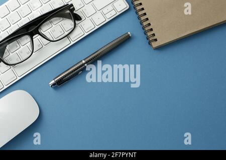 Glasses white keyboard notepad mouse and pen on blue background Stock Photo