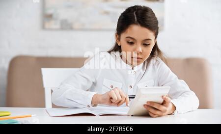 Preteen girl using calculator near notebook and stationery at home Stock Photo