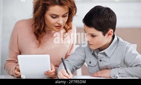 Mother holding digital tablet near son with pen during online education Stock Photo