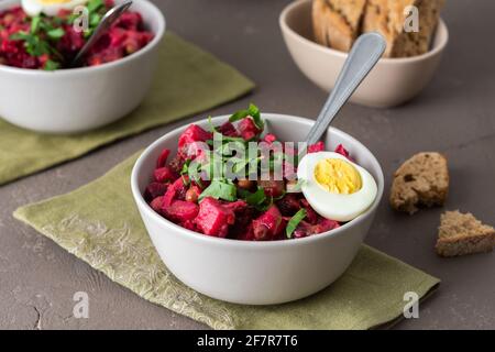 Russian salad vinaigrette in plates with boiled egg and black bread, salad of boiled potatoes and carrots, beetroot and pickled vegetables Stock Photo