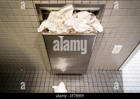 Overflowing paper towel receptacle in a man’s washroom in New York on Friday, March 26, 2021. The NIH has decreed paper towels to be superior to air dryers in public bathrooms as people are more likely to completely dry their hands on paper thus reducing the possibility of bacteria transmission from wet skin. (© Richard B. Levine) Stock Photo