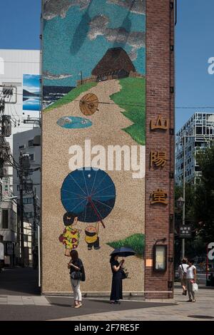 Vertical view of two young women using their mobile phones in front of a giant Japanese mosaic at Omote-Sando with Aoyama-Dori Ave crossing, Harajuku Stock Photo