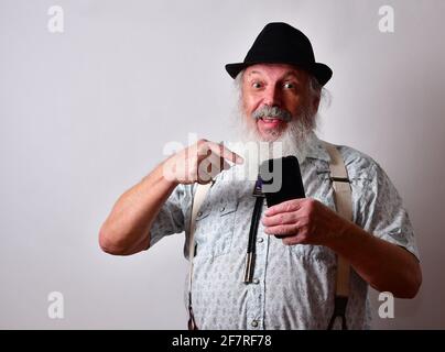 Senior Caucasian bearded male pointing finger on smartphone and smiling Stock Photo