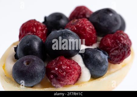 White chocolate egg filled with passion fruit mousse decorated with dried cranberries and fresh blueberries isolated on white Stock Photo