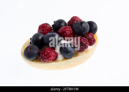 White chocolate egg filled with passion fruit mousse decorated with dried cranberries and fresh blueberries isolated on white Stock Photo