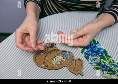 Weaving from beads. Close-up - a woman's hands are stringing beads on a thread, making jewelry. The woman is fond of weaving from beads. Stock Photo