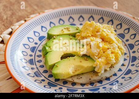 A plate of scrambled eggs served alongside slices of fresh avocado on top of a piece of corn flour bread macro Stock Photo