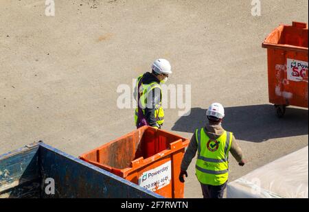 Two labourers wearing hi visibility clothing and white hard hat helmets working on a building site. London. Stock Photo