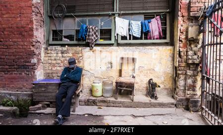 Kolkata, West Bengal, India - January 2018: A security guard sitting beside a grungy brick wall in the city of Kolkata. Stock Photo