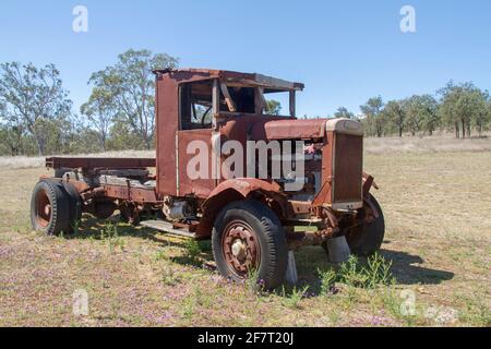 Old and rusting Leyland truck / lorry abandoned in grassy field under blue sky near ruins of historic steam sawmill in Australia Stock Photo