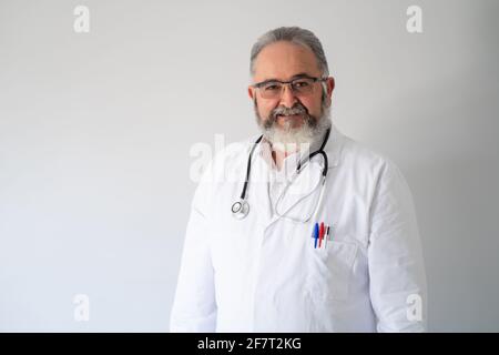 Portrait of senior bearded doctor in white coat and phonendoscope on white background. Stock Photo