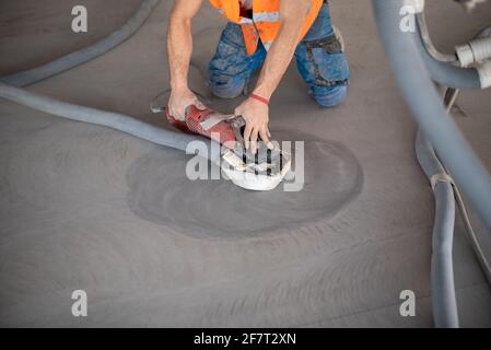 Worker working on the floor of an industrial building. Construction worker producing grout and finishing wet concrete floor. Stock Photo