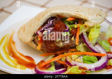 Image of a hamburger seasoned with ketchup, purple onion rings and lettuce on a white plate Stock Photo
