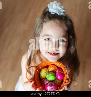 caucasian girl holding multicolored chocolate eggs in a basket and looking upwards into the camera Stock Photo
