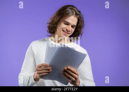 Young handsome man checks documents, utility bills, report. Guy isolated on violet background. He is satisfied Stock Photo