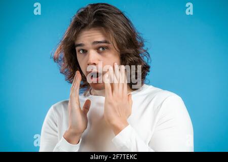 Frightened man shocked isolated on blue background. Stressed and depressed guy with long hairstyle because of bad news Stock Photo