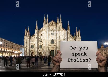 a man holding a sign with the night view of Milan cathedral in the background Stock Photo