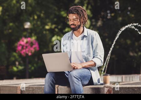 Photo portrait of serious guy working on computer doing project wearing glasses drinking coffee near fountain Stock Photo