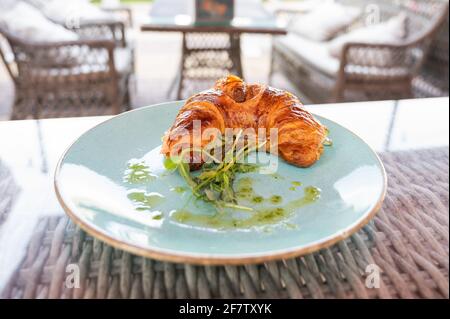 Croissant on a plate on a rattan table in an outdoor cafe. Stock Photo