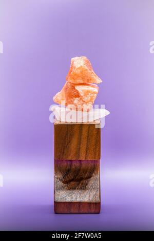 Large chunks of Himalayan sea salt are stacked on top of each other for peace and balance. Supported by a wooden stand and isolated against a purple b Stock Photo