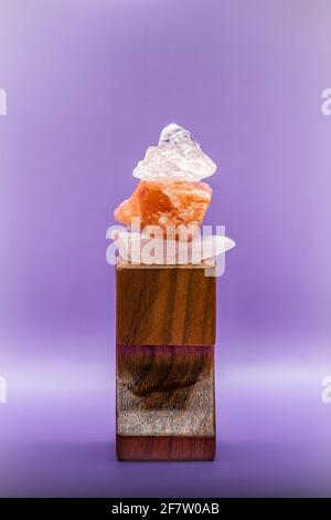Large chunks of Himalayan sea salt are stacked on top of each other for peace and balance. Supported by a wooden stand and isolated against a purple b Stock Photo