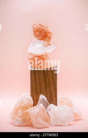 Large chunks of Himalayan sea salt are stacked on top of each other for peace and balance. Supported by a wooden stand and isolated against a soft pin Stock Photo