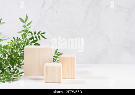 Wooden square podiums with green branch of tree in sunlight on white wood table, marble wall. Fashion showcase for cosmetic products, goods, shoes, ba Stock Photo