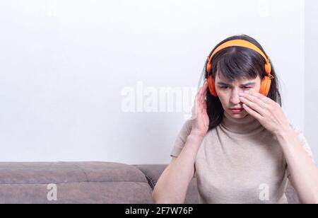 Portrait of a frustrated woman listening to music on a mobile phone and wiping away her tears at home. Woman upset after online communication at home, Stock Photo