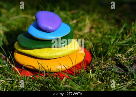 Several brightly colored pebbles painted in rainbow colors lie on top of one another in a meadow with green grass Stock Photo