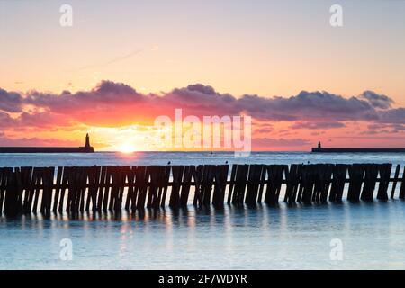 Sunrise at the mouth of the River Tyne captured from the Fish Quay Beach near to Tynemouth Lifeboat Station in North Shields. Old groynes stand in the Stock Photo