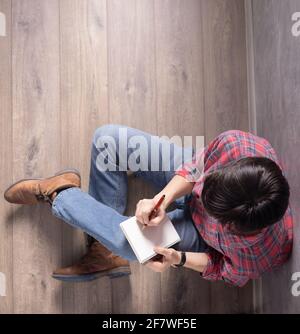 Man sitting on floor thinking with notebook and pen. Student or designer writing in notepad creative concept Stock Photo