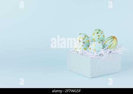 Handmade blue easter eggs with golden glitter design in gift box on blue background. Stock Photo