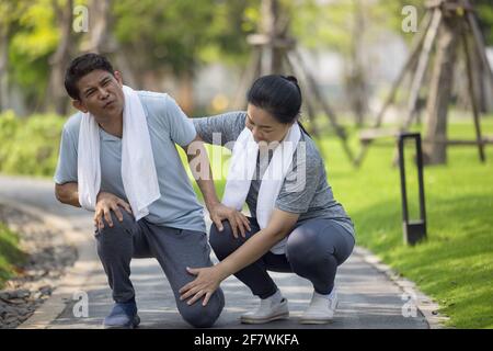 Asian elderly or senior man accident falling down on floor in the park while running exercise have pain knee ache. Stock Photo