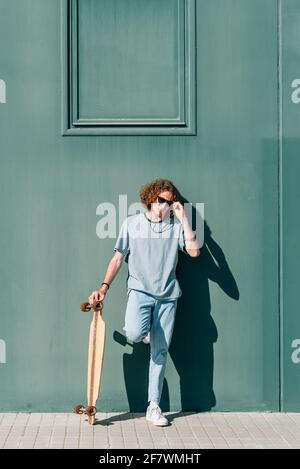 vertical portrait of an attractive young man standing and holding his skateboard. Stock Photo