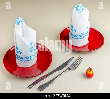A table is set with two red plates with two white napkins decorated in blue on top Stock Photo