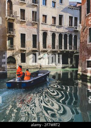 Two orange workers wearing a uniform going to work on boat in Venice, Italy Stock Photo