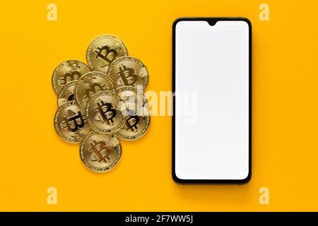 Overhead view of some of bitcoins and mobile phone mockup on a yellow background. Golden BTC coins, Stock Market of cryptocurrencies and decentralized Stock Photo