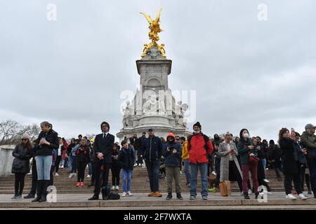 People hold an impromptu silence on the Queen Victoria Memorial outside Buckingham Palace, London, as 41-round Royal gun salutes are fired across the UK, in Gibraltar and at sea, to mark the death of the Duke of Edinburgh at the age of 99.. Picture date: Saturday April 10, 2021. Stock Photo