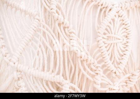 fragment of wall panel in boho style made of cotton threads of natural color using macrame technique for home and wedding decor. Stock Photo