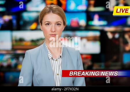 An anchorwoman reporting live breaking news sitting in Tv studio. Background of multiple screens of broadcast control room. Journalism concept Stock Photo