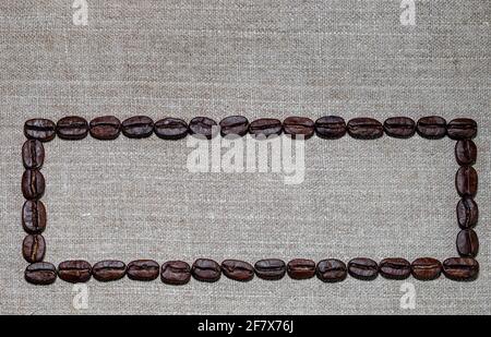 frame lined with black coffee beans on the background of coarse linen cloth Stock Photo